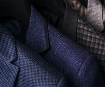 Three patterned suits in shades of blue and gray hang on hangers.