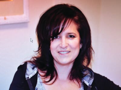 A woman with dark, shoulder-length hair and a slight smile poses indoors against a neutral background.