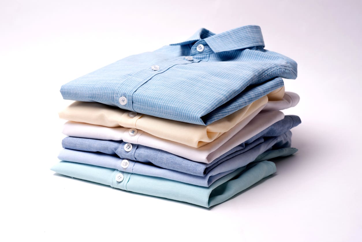 A neatly folded stack of six long-sleeve button-up shirts in various pastel colors on a white background.